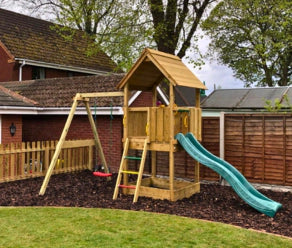 Spielturm aus Holz mit Rutsche und Schaukel im Garten aufgebaut